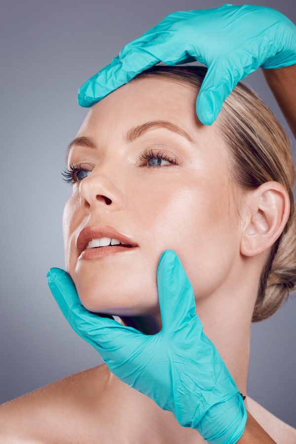 Woman, studio and surgeon hands for cosmetic surgery, facial transformation and beauty by gray back.